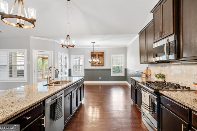 kitchen with dark wood-style flooring, a wainscoted wall, an inviting chandelier, appliances with stainless steel finishes, and a sink