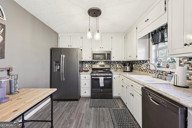 kitchen featuring sink, appliances with stainless steel finishes, hanging light fixtures, white cabinets, and dark hardwood / wood-style flooring