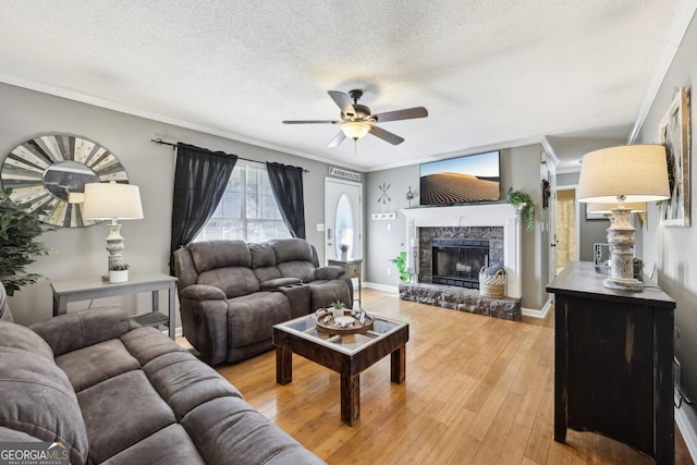 living room featuring a stone fireplace, a textured ceiling, ornamental molding, hardwood / wood-style flooring, and ceiling fan