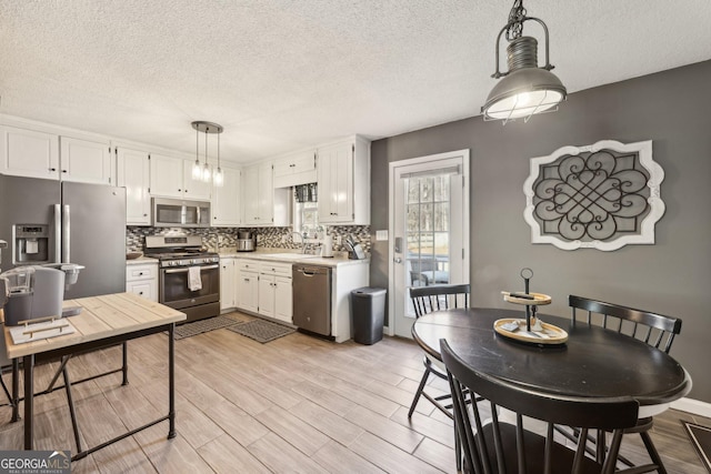 kitchen with appliances with stainless steel finishes, decorative light fixtures, tasteful backsplash, white cabinets, and light hardwood / wood-style floors