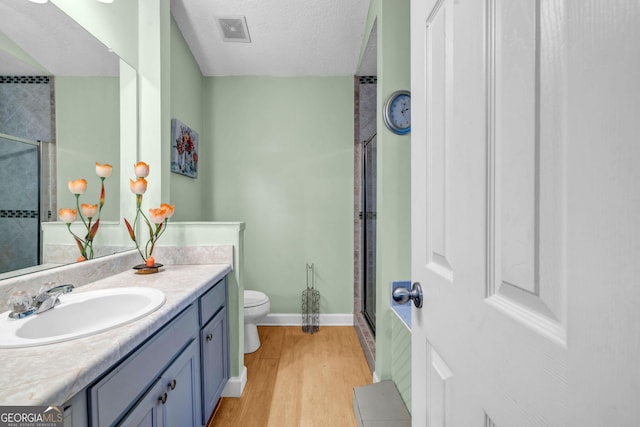 bathroom featuring hardwood / wood-style flooring, vanity, toilet, a shower with door, and a textured ceiling