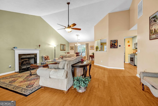 living room with ceiling fan with notable chandelier, high vaulted ceiling, a fireplace, and light hardwood / wood-style floors