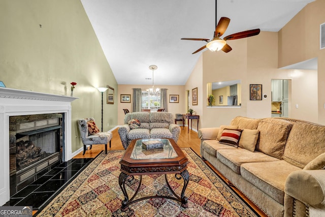 living room with high vaulted ceiling, ceiling fan with notable chandelier, and a high end fireplace