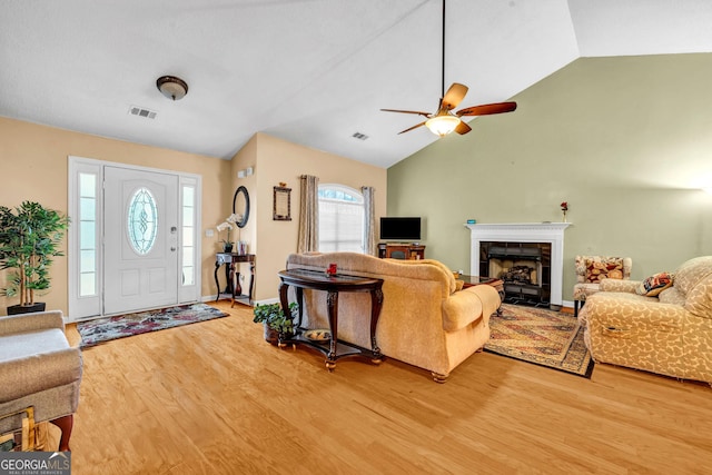 living room with a tile fireplace, lofted ceiling, ceiling fan, and light hardwood / wood-style flooring