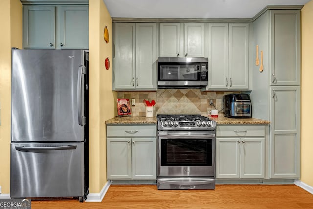 kitchen featuring backsplash, light stone countertops, light hardwood / wood-style floors, and appliances with stainless steel finishes