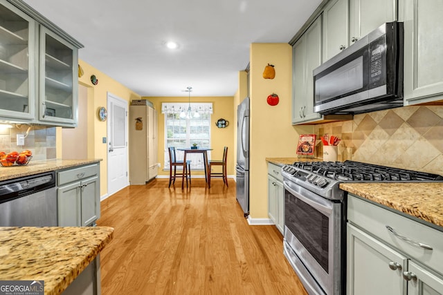 kitchen with appliances with stainless steel finishes, light stone countertops, decorative backsplash, decorative light fixtures, and light wood-type flooring