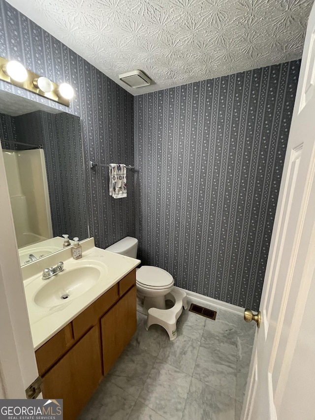 bathroom featuring vanity, a textured ceiling, a shower, and toilet