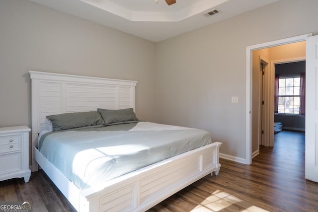 bedroom featuring dark wood-type flooring, a raised ceiling, and ceiling fan