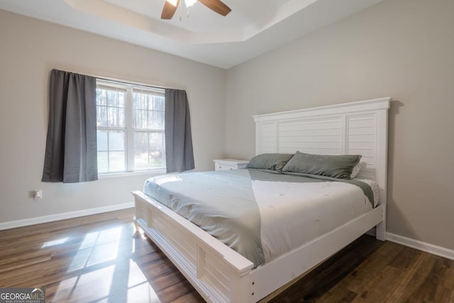 bedroom with dark wood-type flooring, ceiling fan, and a tray ceiling