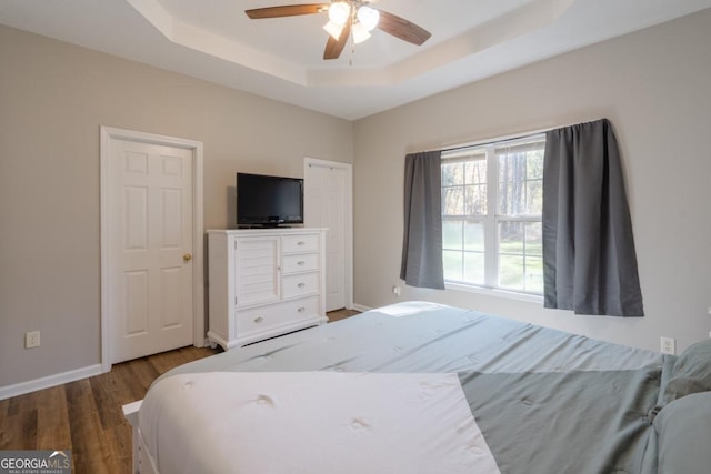 bedroom with wood-type flooring, ceiling fan, and a tray ceiling