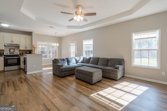 living room with a raised ceiling, ceiling fan with notable chandelier, and light hardwood / wood-style floors