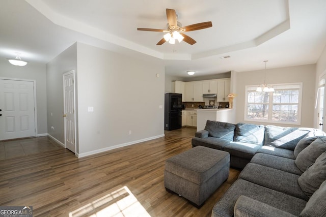 living room with a raised ceiling, wood-type flooring, and ceiling fan with notable chandelier