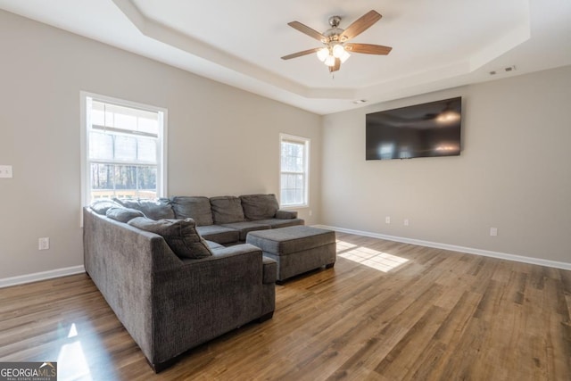 living room with ceiling fan, wood-type flooring, and a raised ceiling