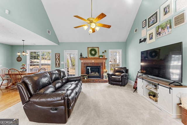 carpeted living room featuring ceiling fan with notable chandelier, a fireplace, and high vaulted ceiling