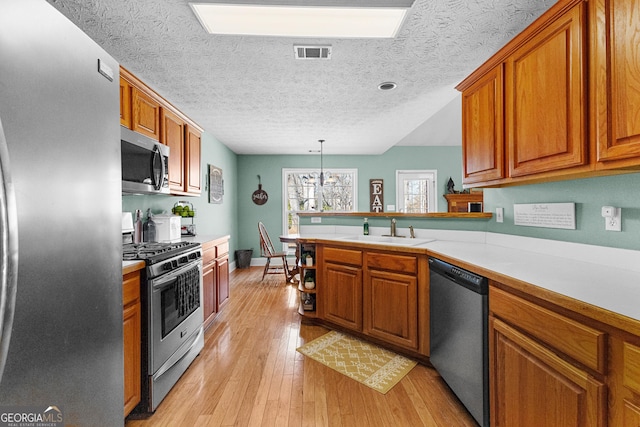 kitchen with sink, hanging light fixtures, stainless steel appliances, light hardwood / wood-style floors, and kitchen peninsula