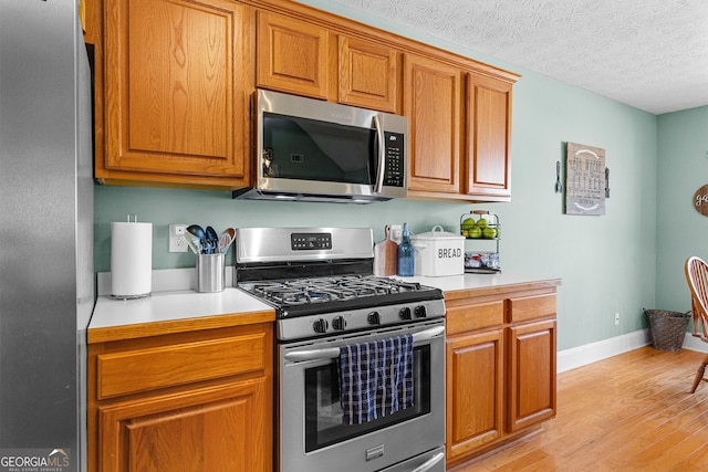 kitchen with stainless steel appliances, a textured ceiling, and light hardwood / wood-style floors