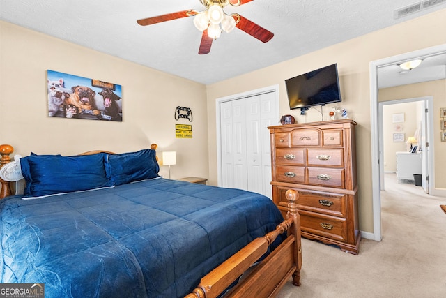 bedroom with ceiling fan, light colored carpet, a closet, and a textured ceiling