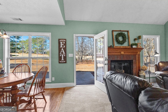 living room with a brick fireplace, a textured ceiling, hardwood / wood-style floors, and a healthy amount of sunlight