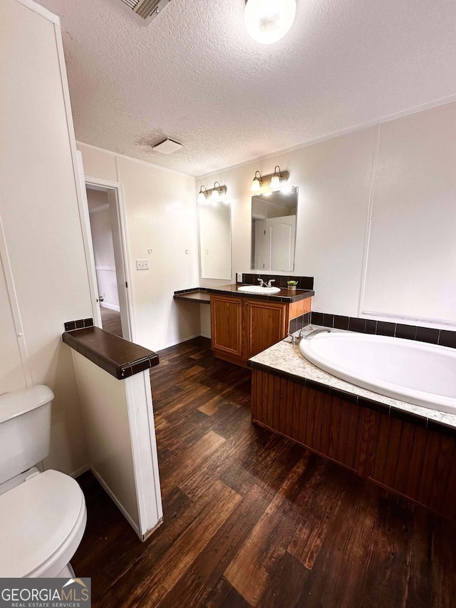 bathroom featuring toilet, a textured ceiling, vanity, a tub, and hardwood / wood-style floors