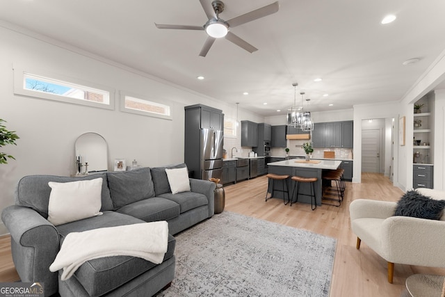 living room with sink, ornamental molding, ceiling fan, and light wood-type flooring