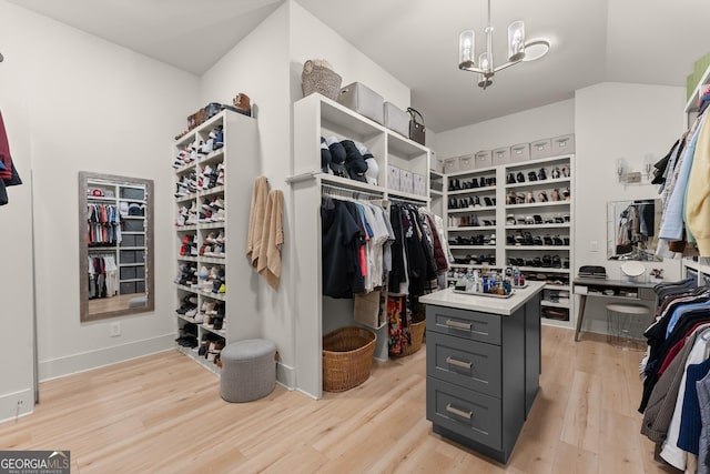 spacious closet with lofted ceiling, light hardwood / wood-style floors, and a chandelier