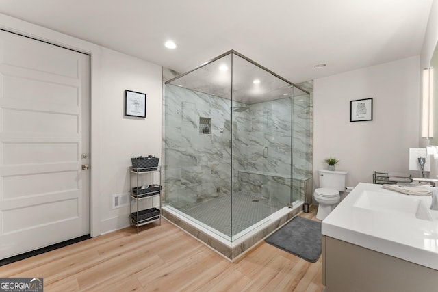 bathroom with wood-type flooring, toilet, a shower with door, and vanity