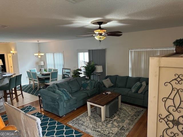 living room featuring hardwood / wood-style floors, ceiling fan with notable chandelier, and a textured ceiling