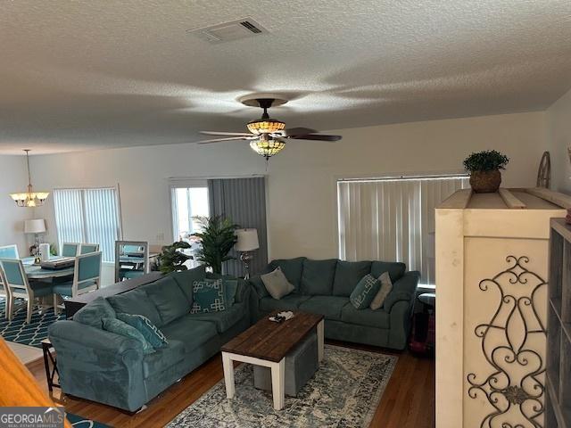 living room with ceiling fan with notable chandelier, dark hardwood / wood-style floors, and a textured ceiling