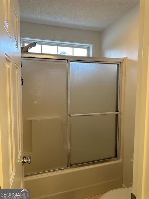 bathroom with a textured ceiling, bath / shower combo with glass door, and toilet