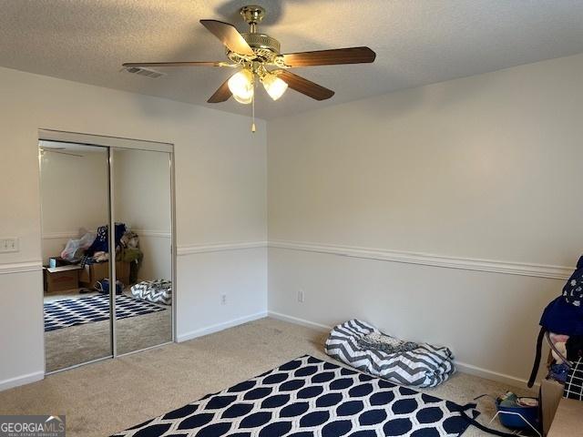 bedroom featuring ceiling fan, light carpet, a closet, and a textured ceiling