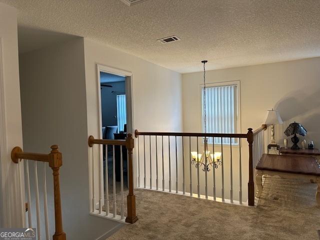 corridor featuring carpet flooring, a notable chandelier, and a textured ceiling