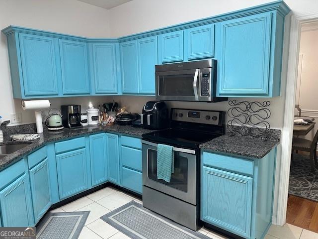 kitchen featuring light tile patterned flooring, appliances with stainless steel finishes, blue cabinets, and dark stone counters