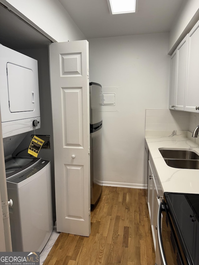 washroom with stacked washer / drying machine, sink, and light hardwood / wood-style flooring