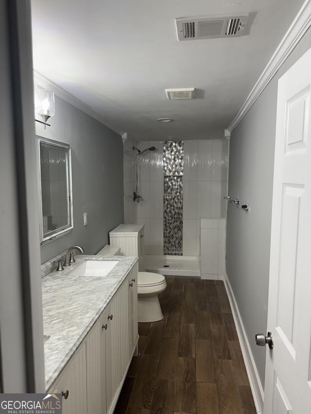 bathroom featuring hardwood / wood-style flooring, ornamental molding, toilet, and a tile shower