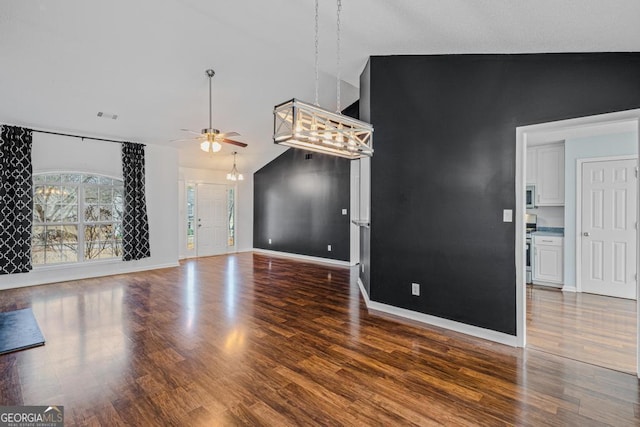 unfurnished living room featuring high vaulted ceiling, dark hardwood / wood-style flooring, and ceiling fan with notable chandelier