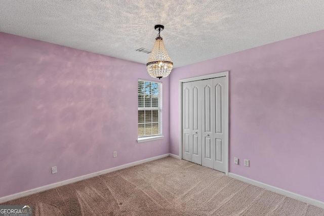 unfurnished bedroom with a notable chandelier, carpet floors, a closet, and a textured ceiling