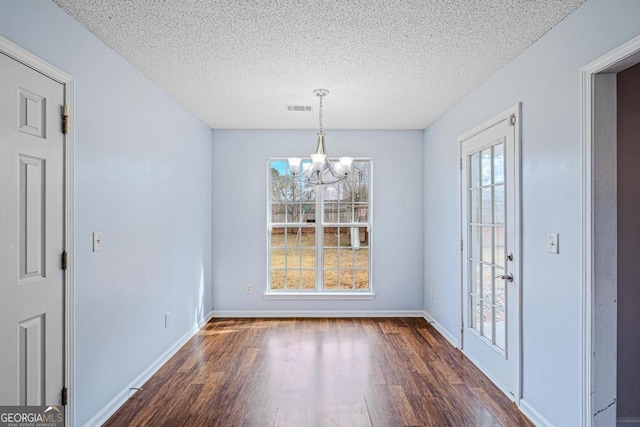 unfurnished dining area featuring dark hardwood / wood-style flooring, a textured ceiling, and a notable chandelier