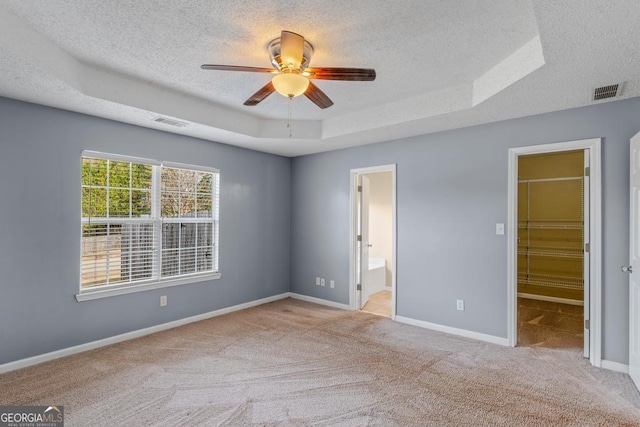 unfurnished bedroom featuring a raised ceiling, a spacious closet, and a textured ceiling