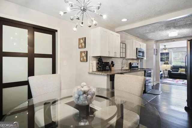 dining area with sink, ceiling fan with notable chandelier, dark wood-type flooring, and a textured ceiling