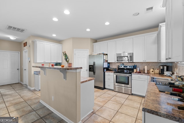 kitchen with appliances with stainless steel finishes, white cabinetry, sink, a kitchen bar, and a center island