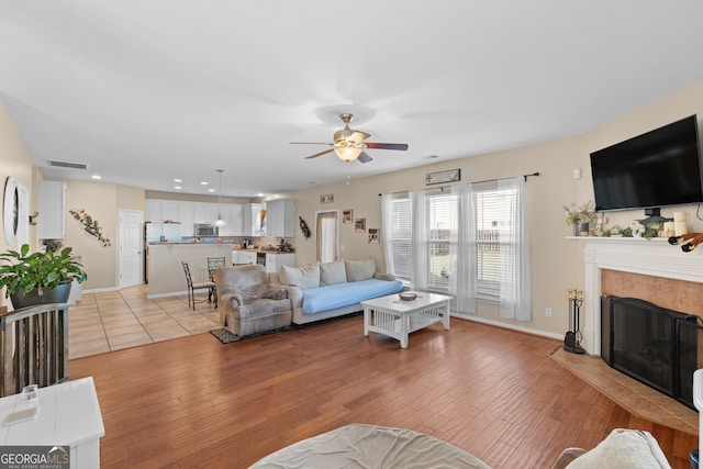 living room with a premium fireplace, ceiling fan, and light wood-type flooring