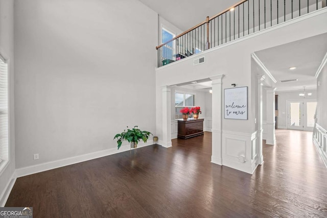 interior space featuring crown molding, a healthy amount of sunlight, dark hardwood / wood-style flooring, and ornate columns