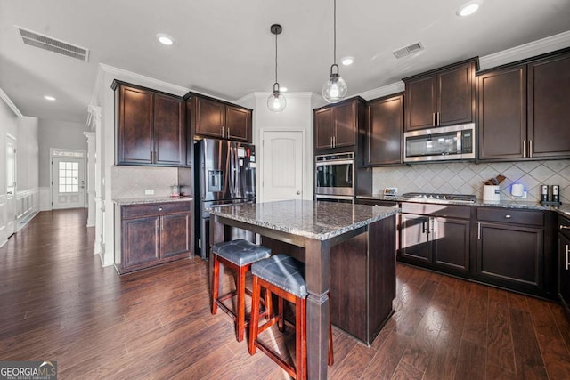 kitchen with a breakfast bar, stainless steel appliances, a center island, decorative light fixtures, and dark stone counters