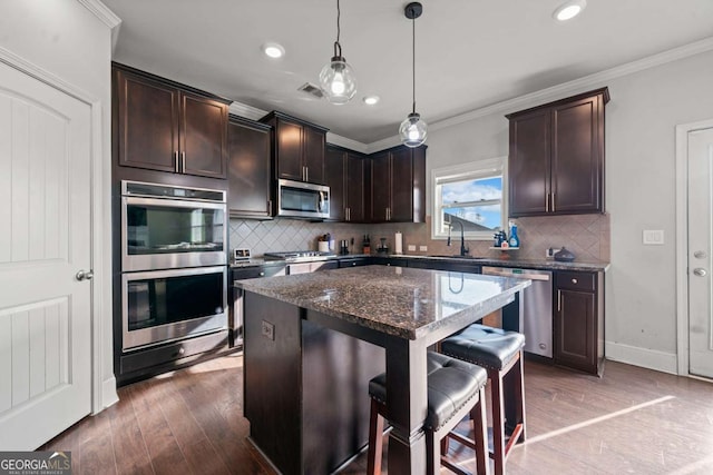 kitchen featuring pendant lighting, a breakfast bar, appliances with stainless steel finishes, a center island, and dark stone counters