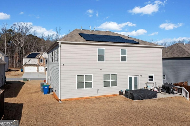 back of house featuring a yard, a patio area, and solar panels