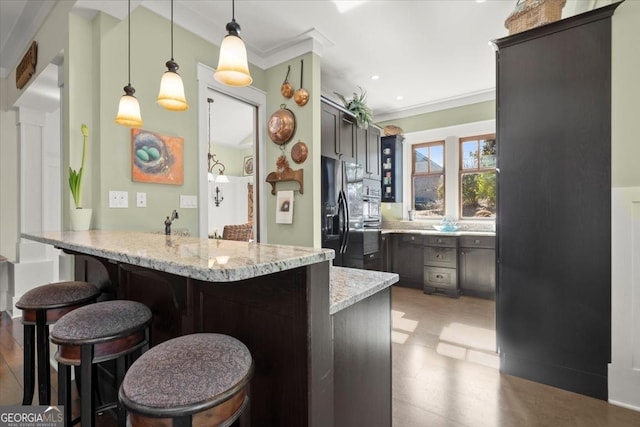 kitchen with black fridge, light stone countertops, a kitchen bar, decorative light fixtures, and kitchen peninsula