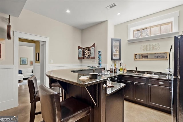 kitchen featuring dark brown cabinetry, a breakfast bar area, black refrigerator, a kitchen island, and dark stone counters