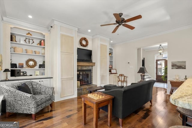 living room with built in shelves, ornamental molding, dark hardwood / wood-style floors, and a stone fireplace