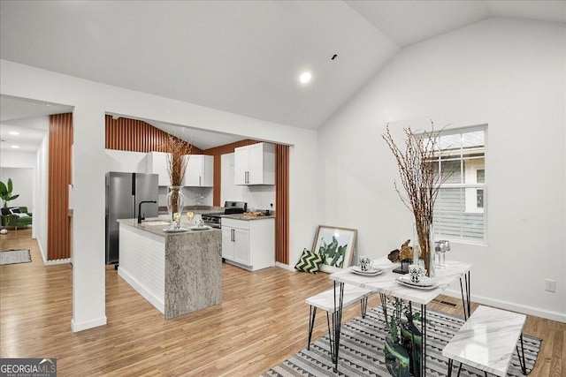 interior space featuring white cabinetry, vaulted ceiling, light wood-type flooring, appliances with stainless steel finishes, and a kitchen island with sink