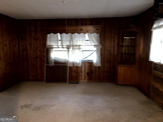 unfurnished dining area featuring light carpet and wood walls